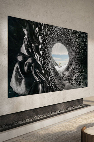 Large thin TV screen mounted on a wall with a modern fire place underneath. TV features picture from the inside of a wave in the ocean with a surfer on a surfboard.