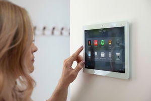 Woman with hand touching a control panel on the wall showcasing the Control4 app which highlights lighting and other technologies. Message on the picture says Lighting Control Brand Partners curated for cutting edge tech and support. 