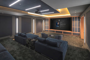 Large Home Theater with gray suede couches and seats. Large theater screen displaying Avatar movies description. A projector is mounted on ceiling projecting on to screen. There are specialty theater lights in ceiling and on walls. 